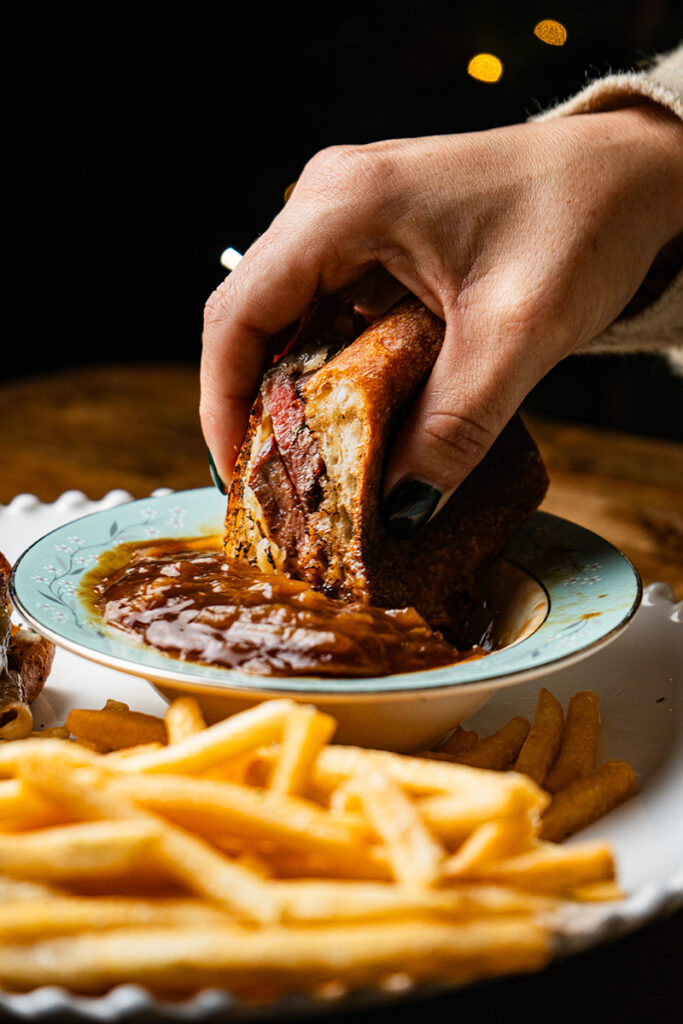 Hand dipping sandwich into sauce