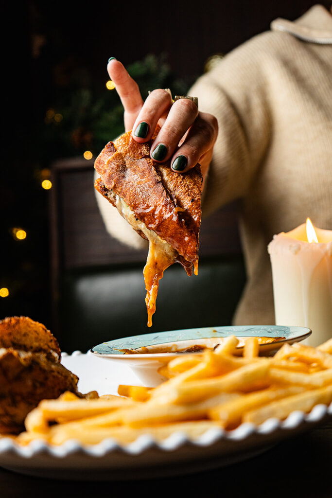 Hand holding cheesy sandwich with fries